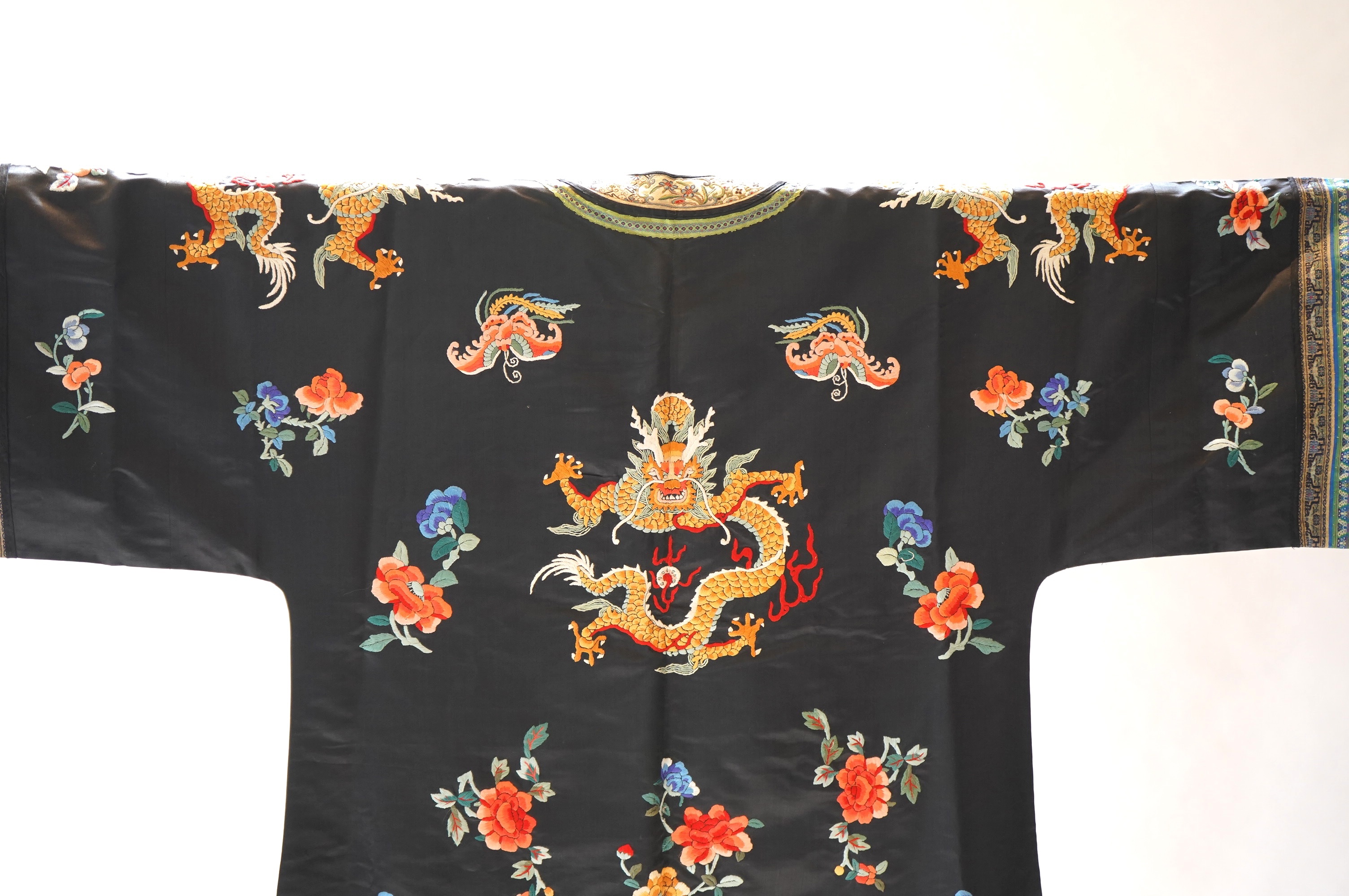 An early 20th century Chinese blue satin silk embroidered dragon robe, embroidered with five claw dragon symbols with flaming pearls, surrounded by bats and flower motifs, with gold thread embroidered dragon sleeve bands